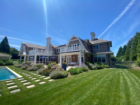 Luxury multi-story home with manicured lawn, swimming pool, and landscaped gardens under blue sky