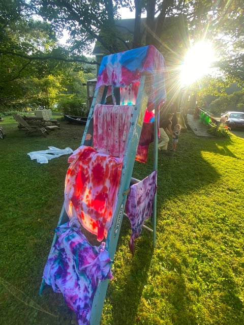 Colorful tie-dye fabrics hanging on a wooden ladder in a sunny park with green grass and trees