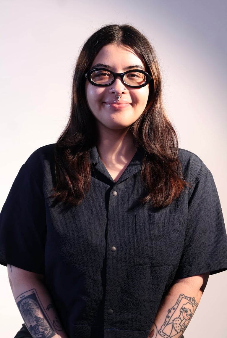 Woman with long dark hair and glasses wearing a black short-sleeved button-up shirt, smiling at the camera
