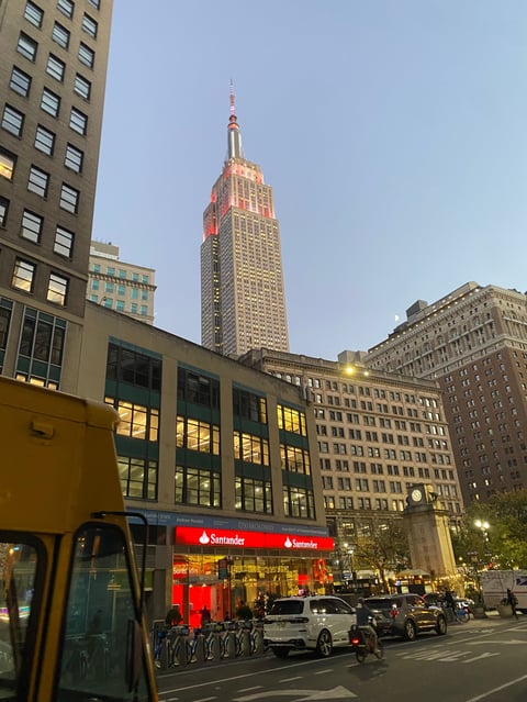 Empire State Building towering above Manhattan street with Santander bank storefront and yellow taxi in foreground