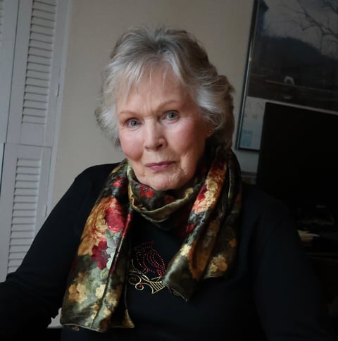 Older woman with gray hair wearing a black top and colorful floral scarf, seated indoors